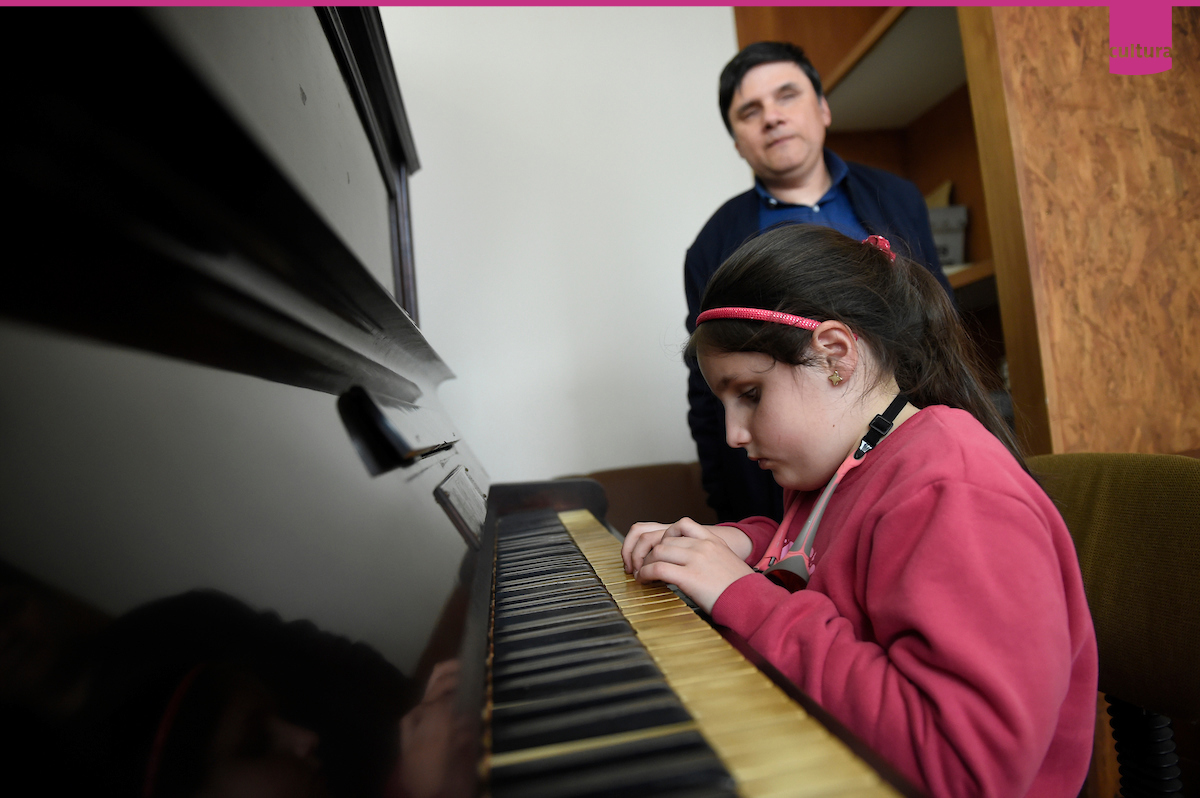 niña toca piano y adulto escucha
